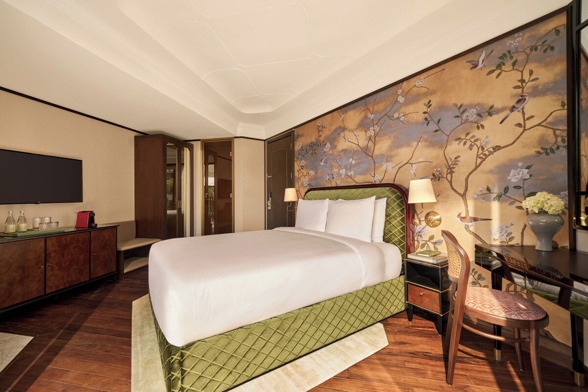 A hotel room with a large bed, a desk with a chair, a TV, and a decorative wall.