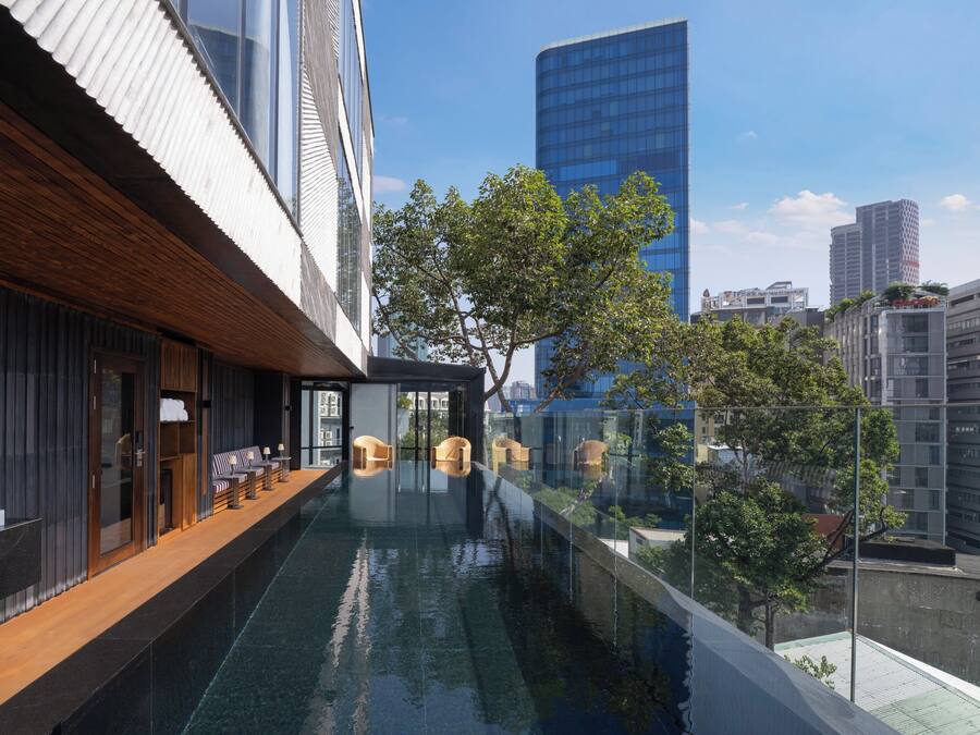 Un hotel moderno con piscina infinita en la azotea, asientos en terraza de madera y vistas al horizonte de la ciudad.