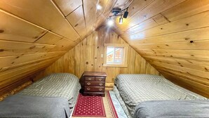 A cozy attic bedroom with two beds, a wooden dresser, and a small window.