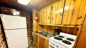 A compact kitchen with wooden cabinets, a white refrigerator, a stove, and a sink.
