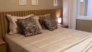 A neatly made bed with a beige quilt, two patterned pillows, and a bedside table with a lamp.