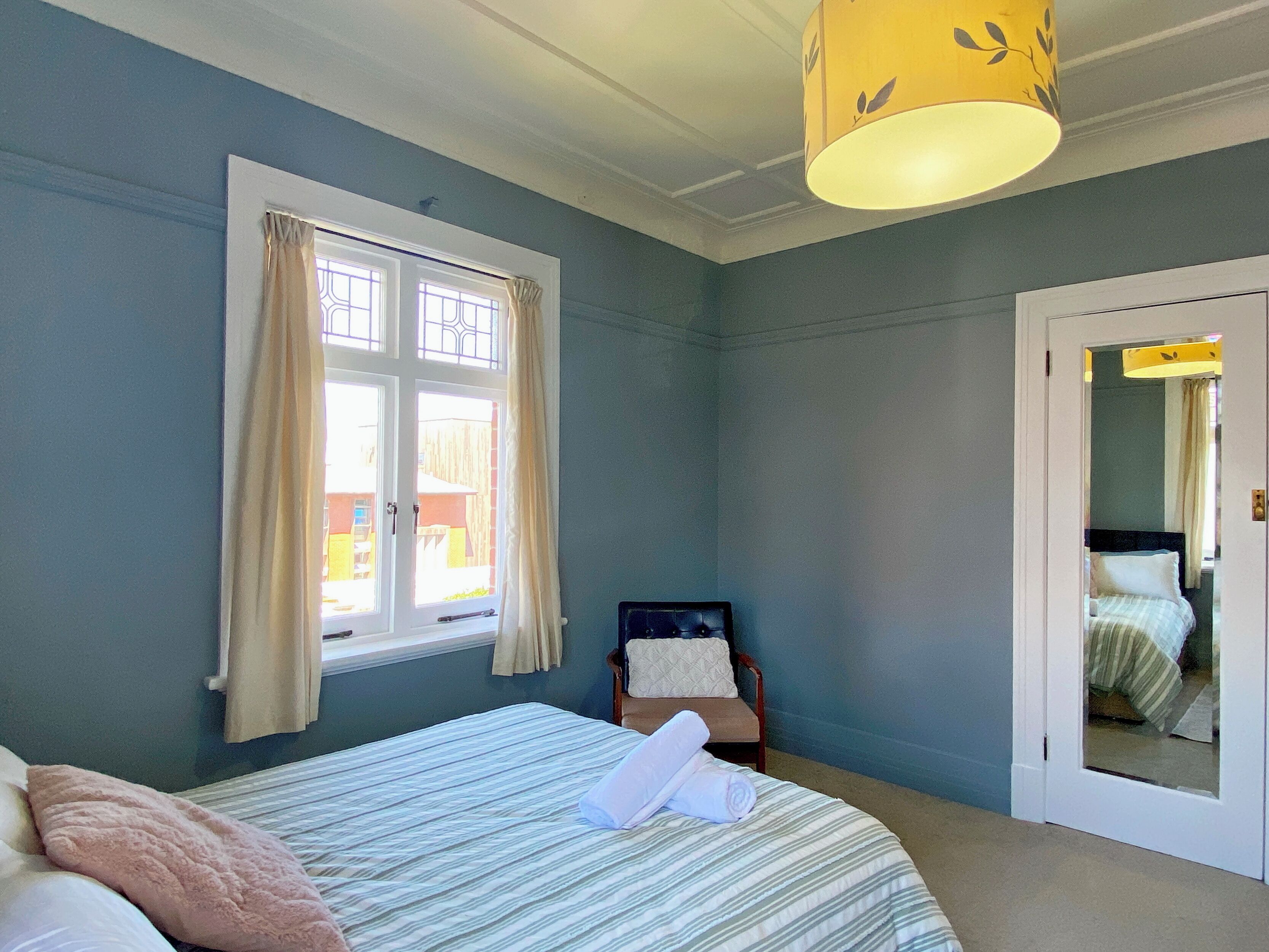 Une chambre à coucher avec un lit, une chaise, une fenêtre avec des rideaux et une porte donnant sur une autre pièce.