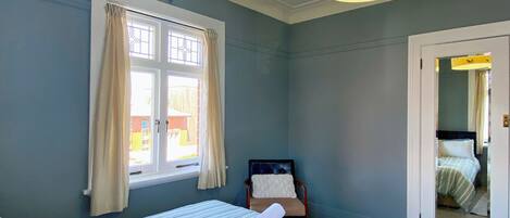 Une chambre à coucher avec un lit, une chaise, une fenêtre avec des rideaux et une porte donnant sur une autre pièce.