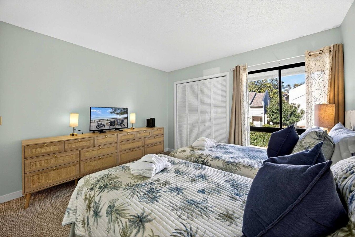 Camera d'albergo con due letti, una TV, una cassettiera in legno e una finestra con tende.