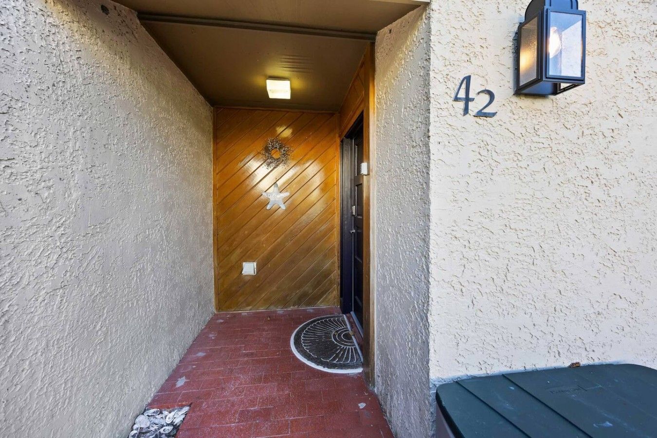 Un couloir étroit avec une porte en bois, une plaque portant le numéro « 42 » et un luminaire fixé au mur.