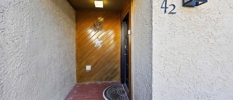A narrow hallway with a wooden door, a number '42' sign, and a wall-mounted light fixture.