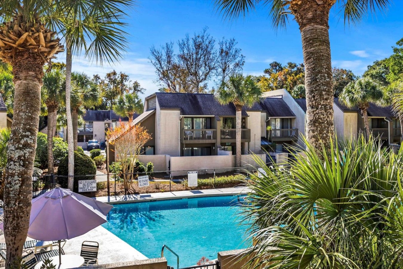 A pool area with a clear blue pool, surrounded by palm trees and a building with balconies.