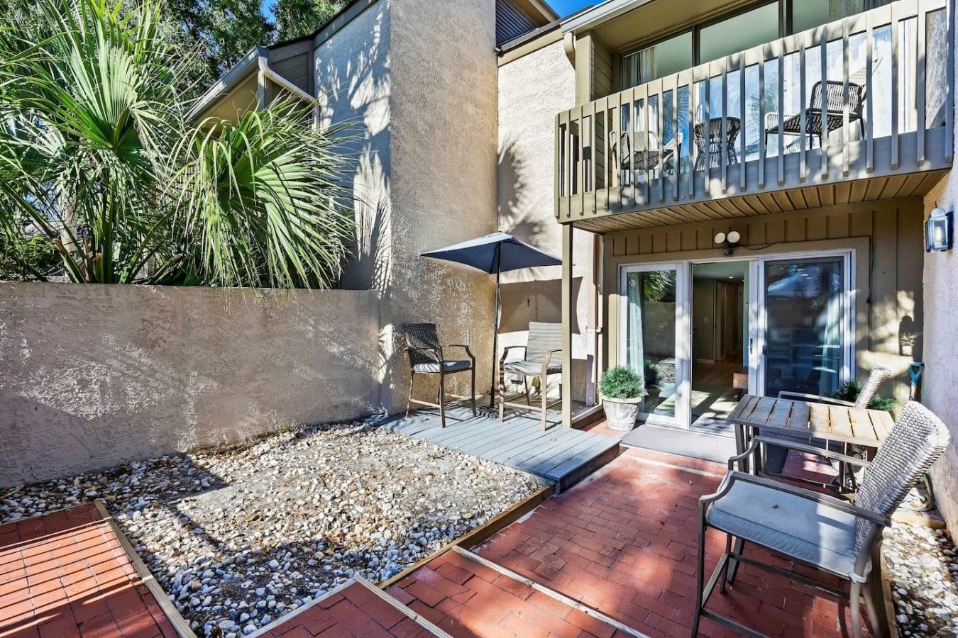 A patio area with a table and chairs, a small garden with pebbles, and a balcony with outdoor furniture.