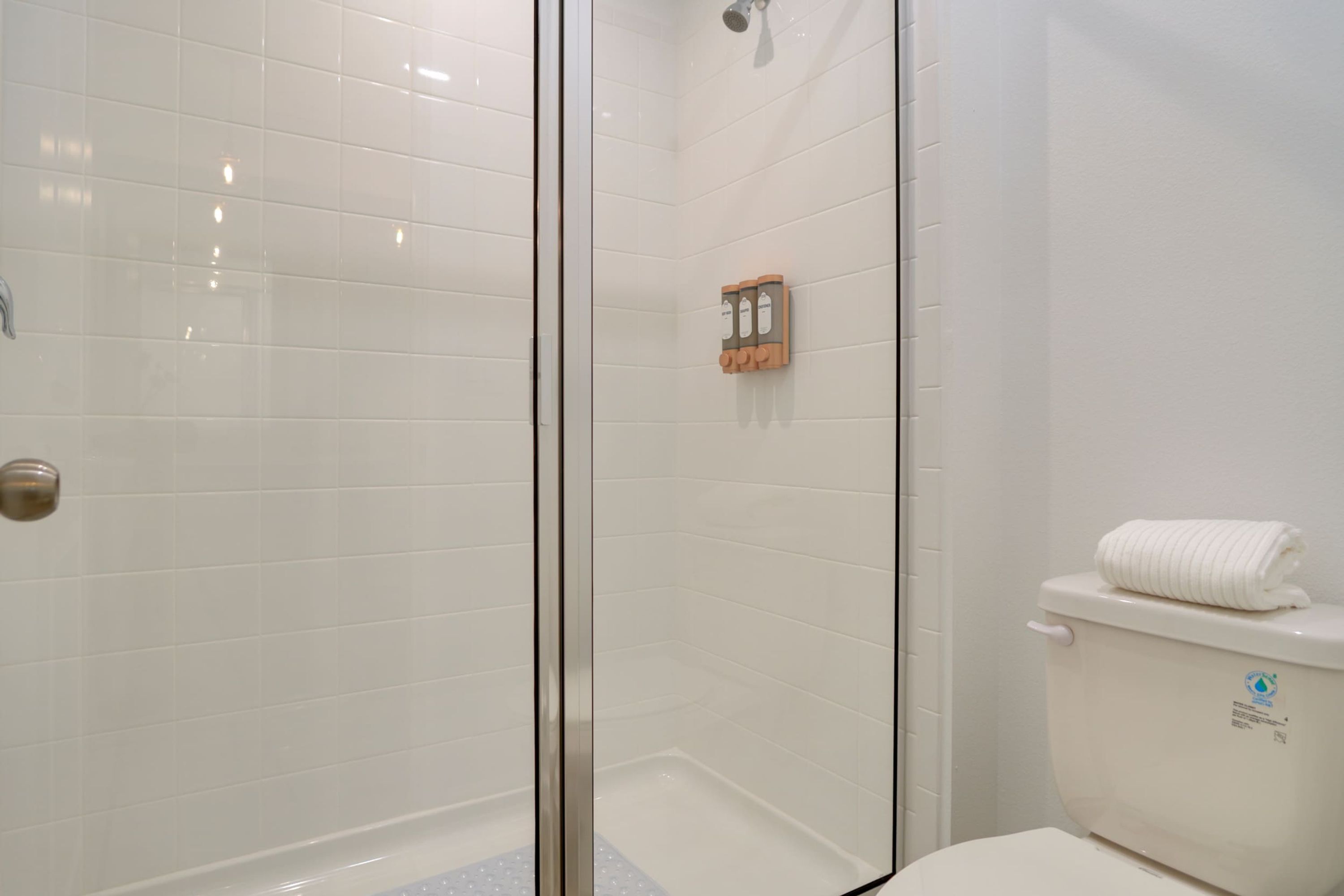 A bathroom with white tiled walls, a glass shower enclosure, a toilet, and a towel rack.