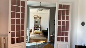Een kamer met een brede open doorgang naar een andere kamer, een radiator, een kamerbreed tapijt en een spiegel aan de muur.