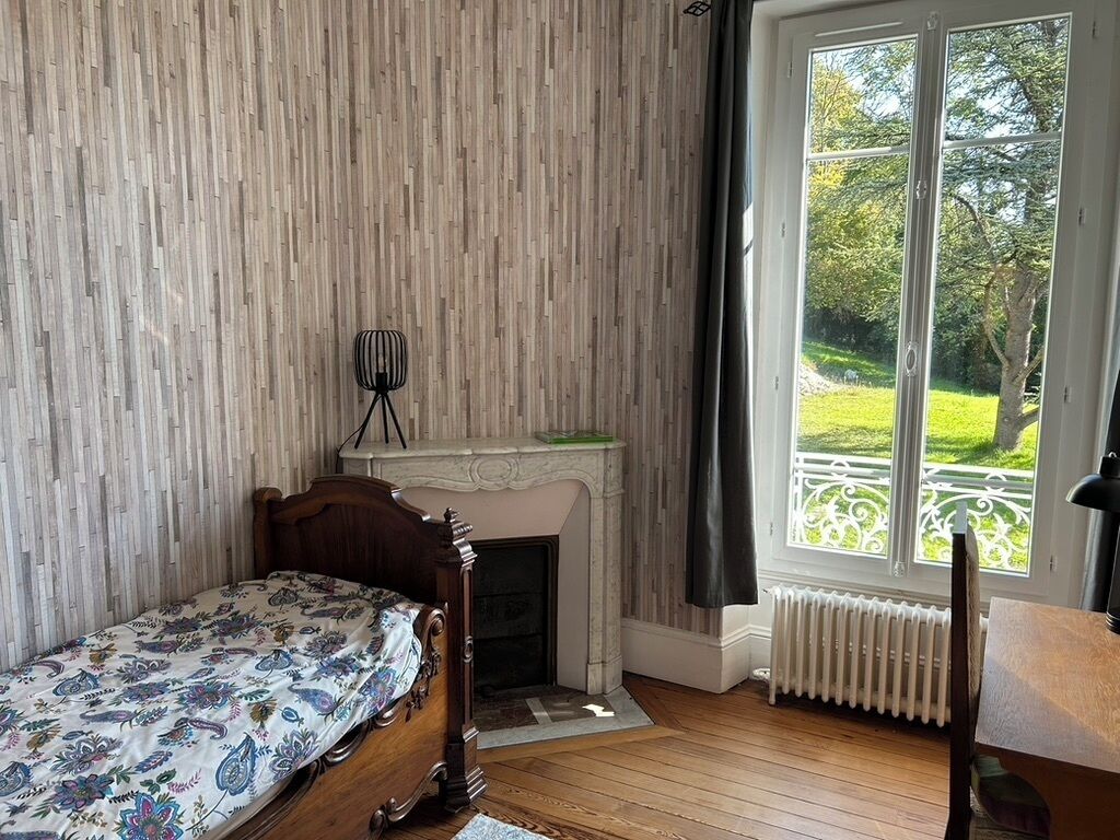 A bedroom with a wooden bed, a fireplace, a radiator, and a window with a view of a garden.