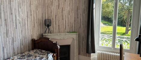 A bedroom with a wooden bed, a fireplace, a radiator, and a window with a view of a garden.