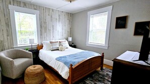 A bedroom with a wooden bed, a chair, a desk, and two windows with blinds. - Downtown Waterville Studio Apt|Washer/Dryer (Waterville)