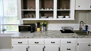 A kitchen with white cabinets, a granite countertop, a microwave, a sink, and a window with blinds. - Downtown Waterville Studio Apt|Washer/Dryer (Waterville)