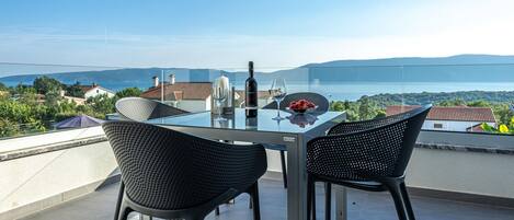 Et glasbord med to stole på en balkon med udsigt over et smukt hav og bakkelandskab.