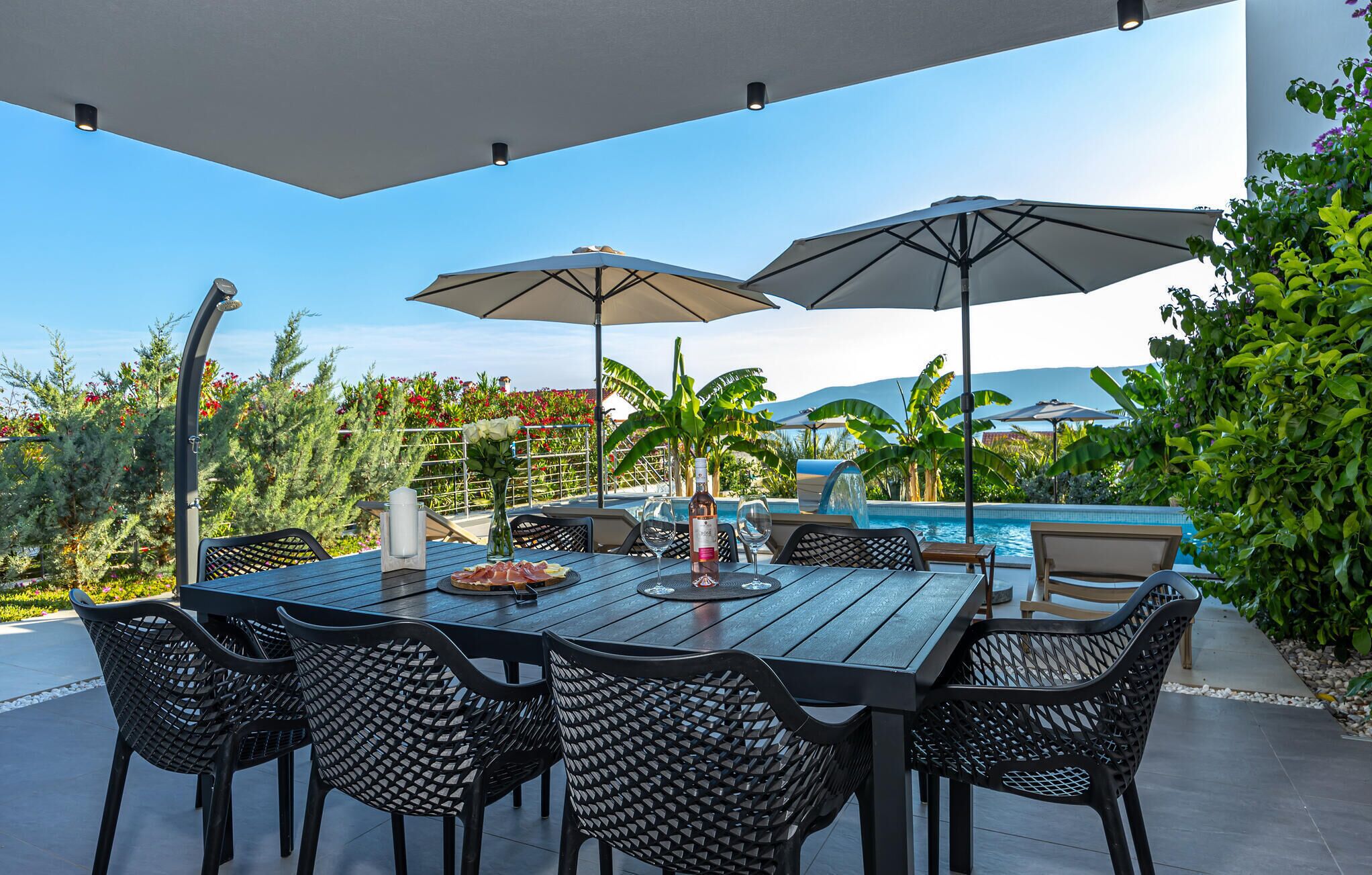 An outdoor dining area with a pool view, featuring a table with chairs and umbrellas.