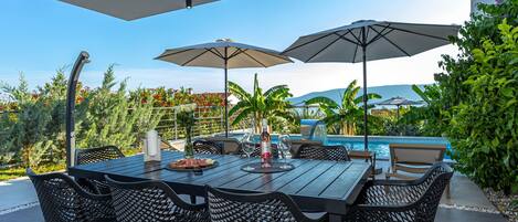 An outdoor dining area with a pool view, featuring a table with chairs and umbrellas.