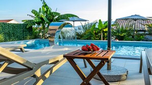 Ein Poolbereich mit Holztisch, Liegestühlen und einem Wasserfall.