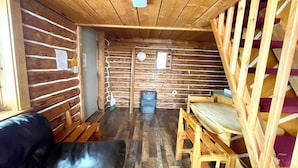 A log cabin interior with a wooden bench, a black leather sofa, and a wooden table. - Fisherman's Fortress — Rustic Cabin (Delta Junction)