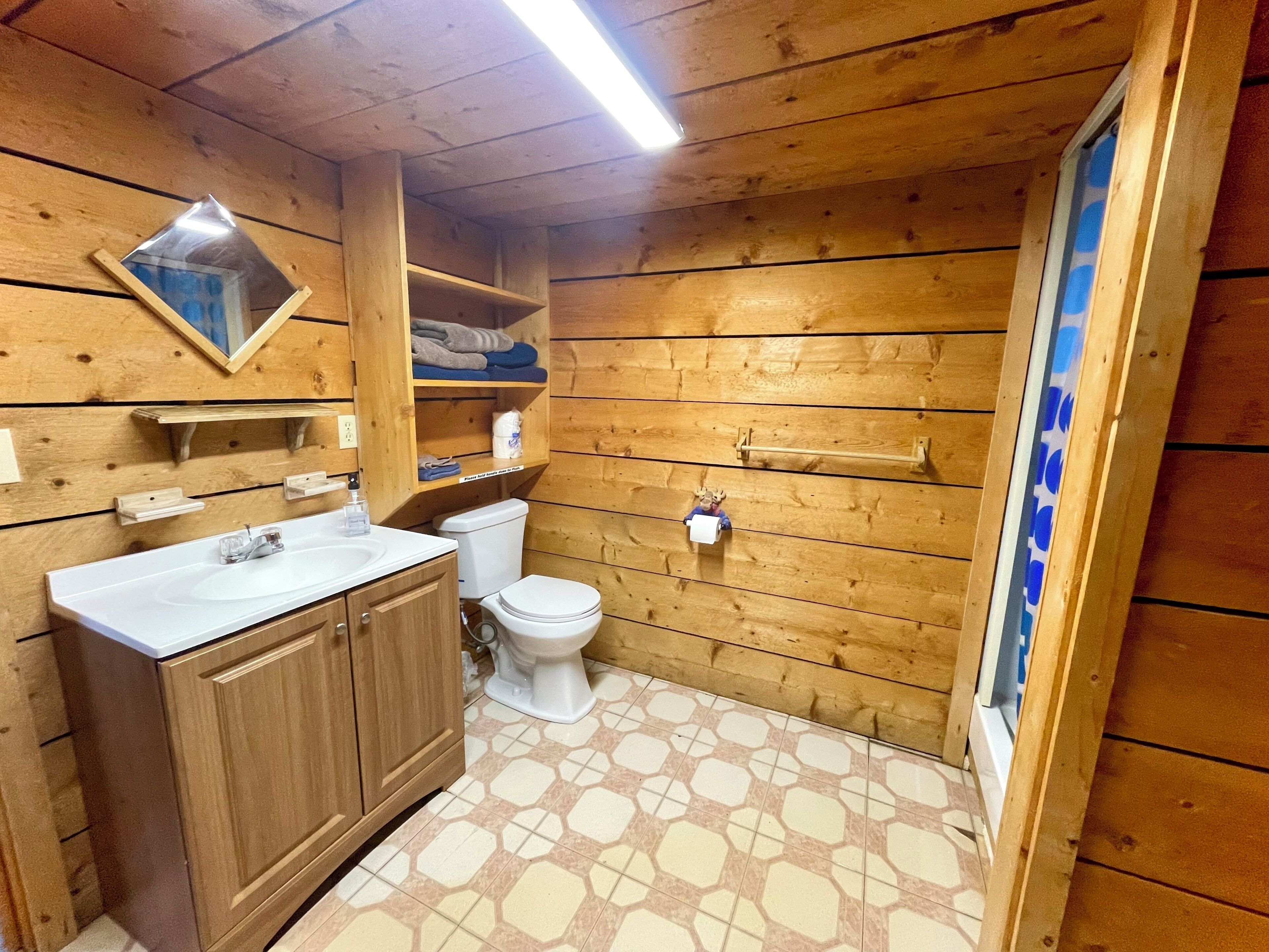 Un bagno con rivestimenti in legno, un lavandino, un water e mensole.
