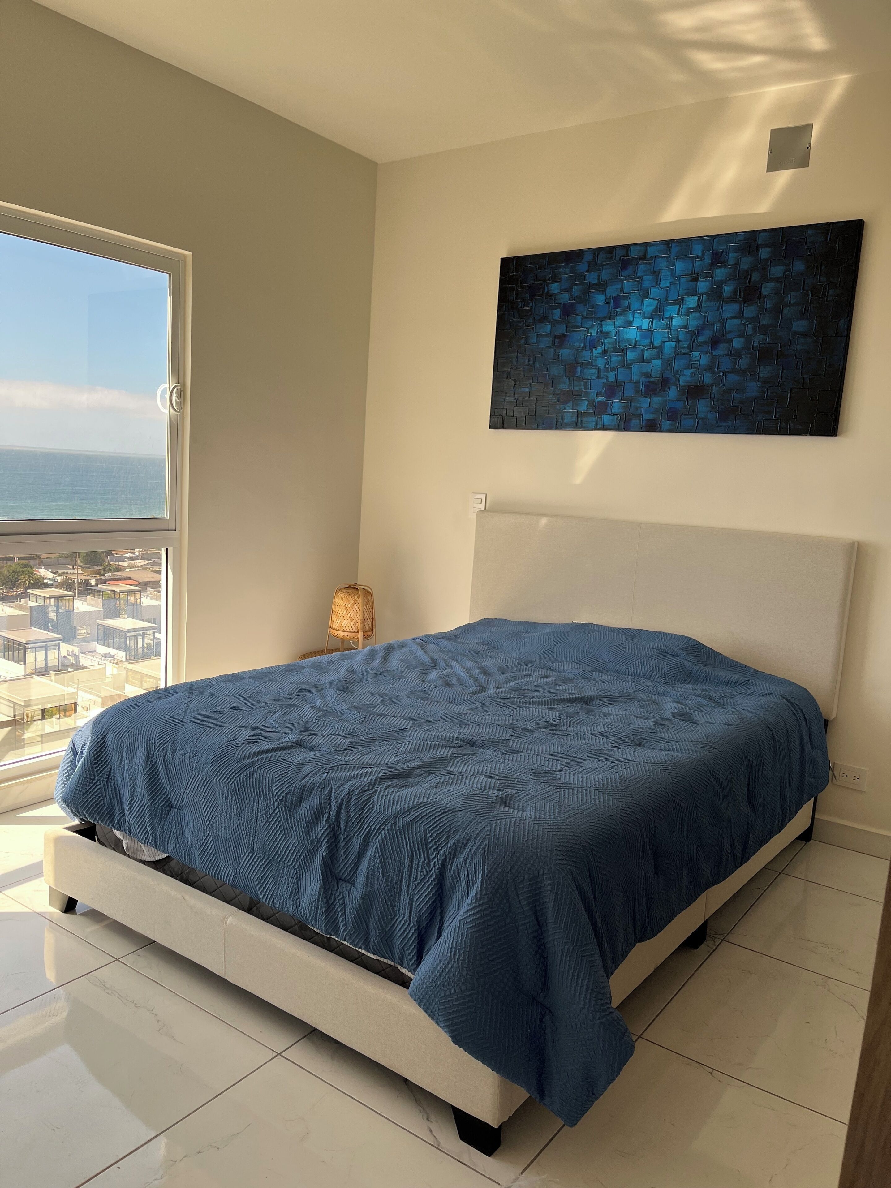 Quarto com cama, vista da cidade e uma janela grande.