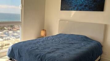 Quarto com cama, vista da cidade e uma janela grande.