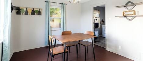 A dining area with a wooden table and chairs, a chandelier, and a kitchen visible through an open doorway.