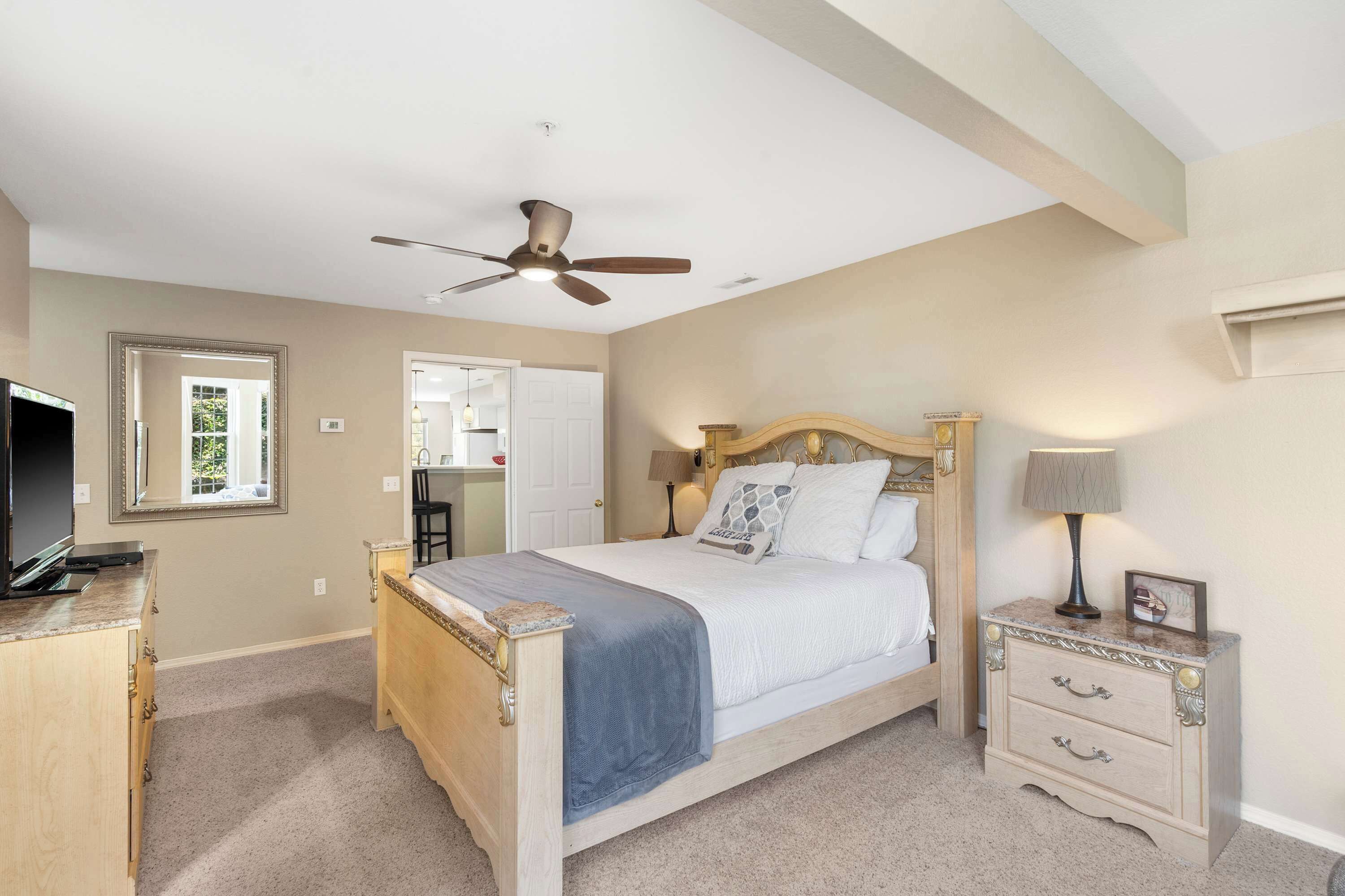 A bedroom with a bed, a nightstand, a ceiling fan, and a television on a dresser.