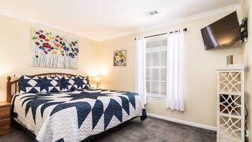 A bedroom with a bed, a nightstand, a TV mounted on the wall, and a window with curtains.