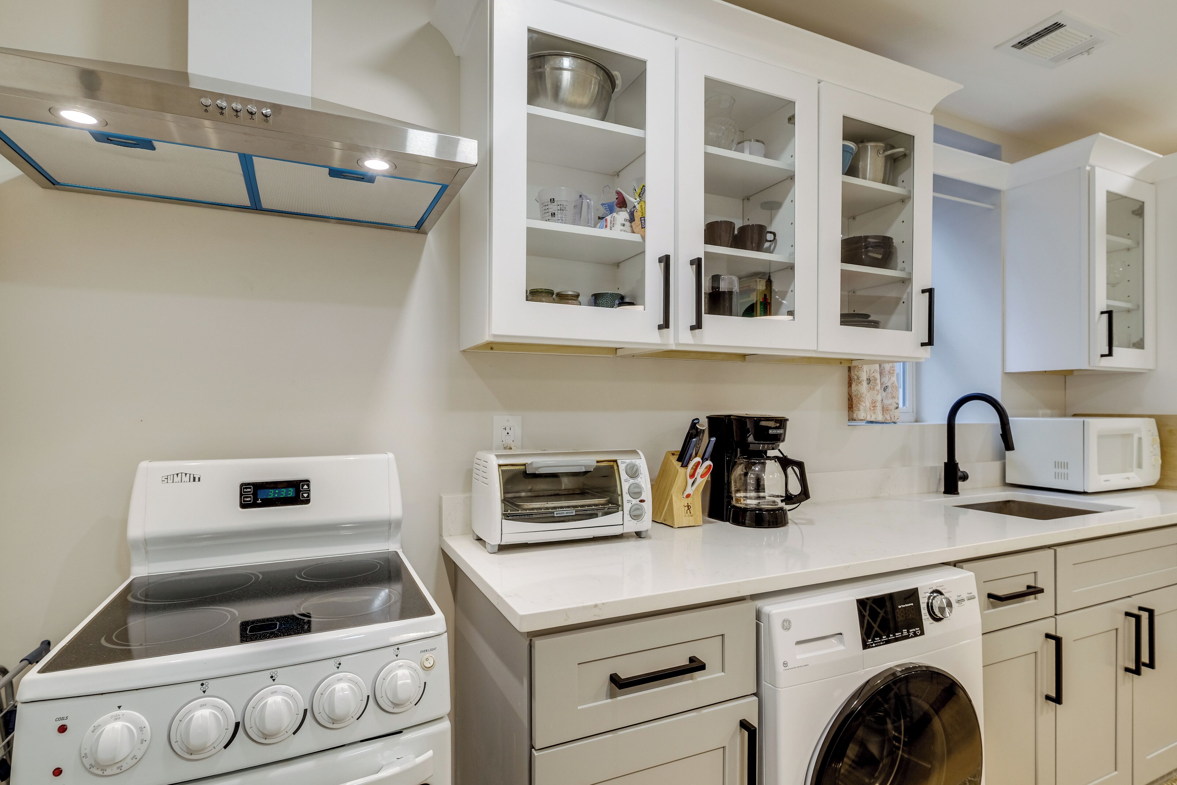 Een moderne keuken met witte kasten, een inbouwoven, een magnetron, een broodrooster en een wasmachine.