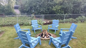 Uma fogueira rodeada por quatro cadeiras Adirondack azuis numa área gramada ao ar livre.