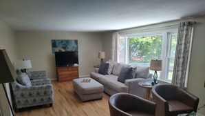 Uma sala de estar com sofá, duas poltronas, mesa de centro, televisão e abajur.
