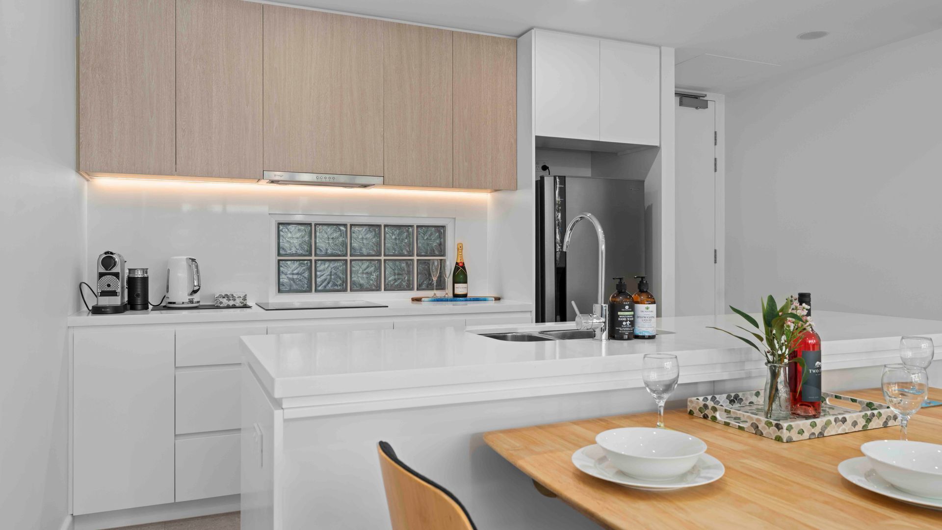A modern kitchen with white cabinetry, a built-in island, and a dining area with a wooden table.