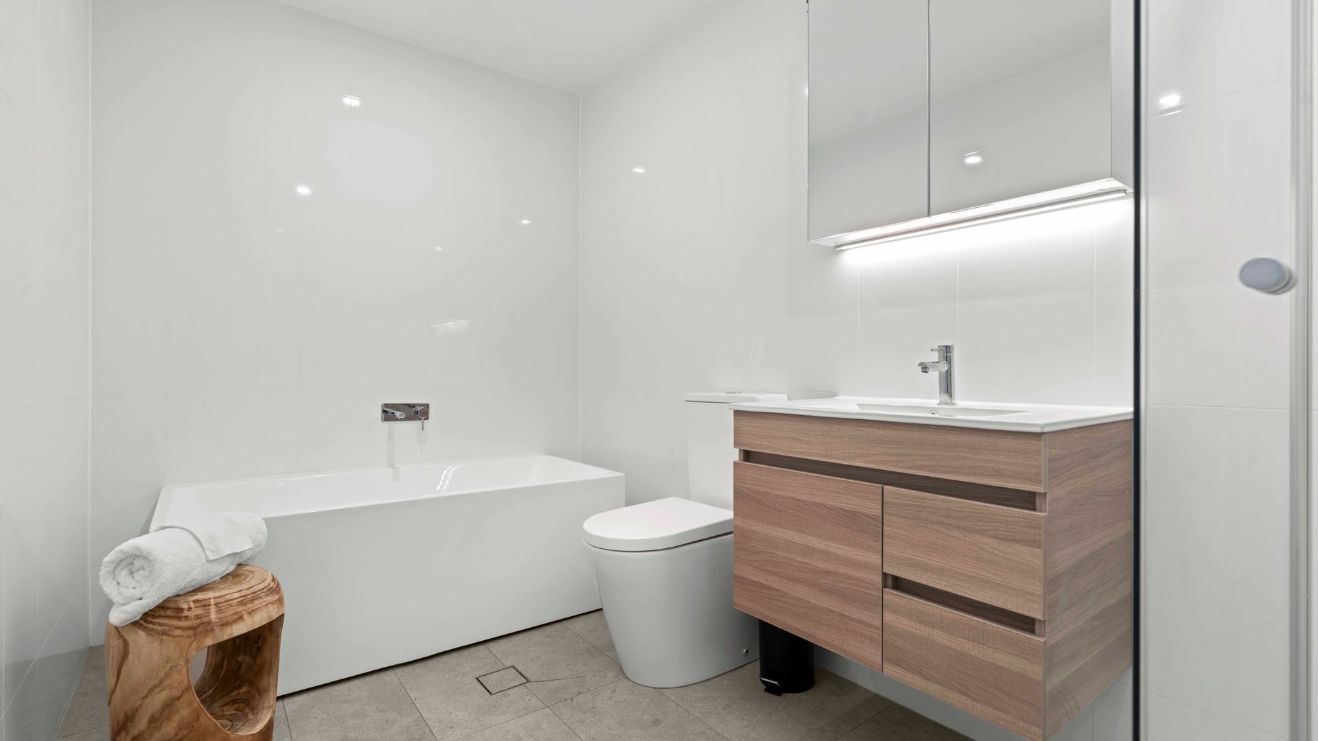 A modern bathroom with a white bathtub, a toilet, and a vanity with a mirror.