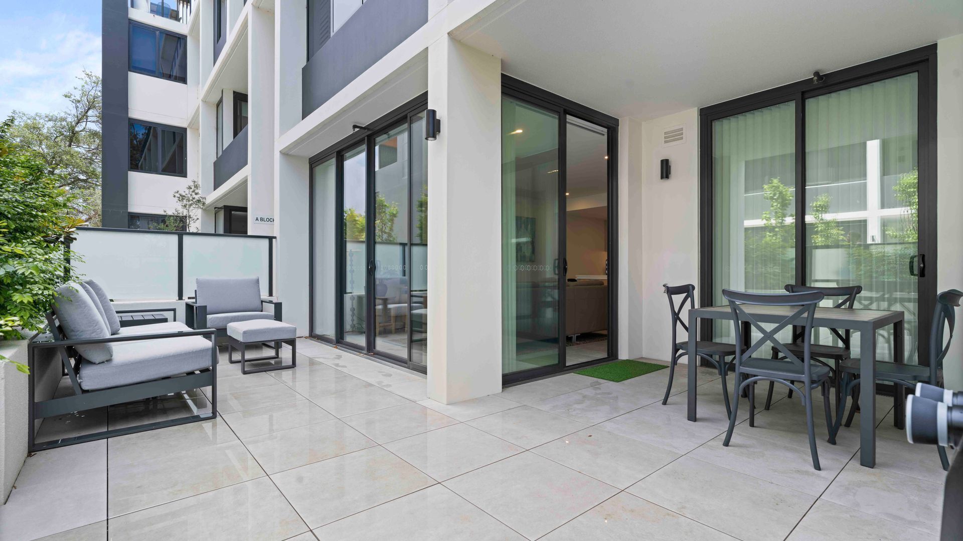 A modern outdoor patio area with a sofa set, a dining table with chairs, and a sliding glass door leading to a balcony.