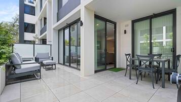 A modern outdoor patio area with a sofa set, a dining table with chairs, and a sliding glass door leading to a balcony.