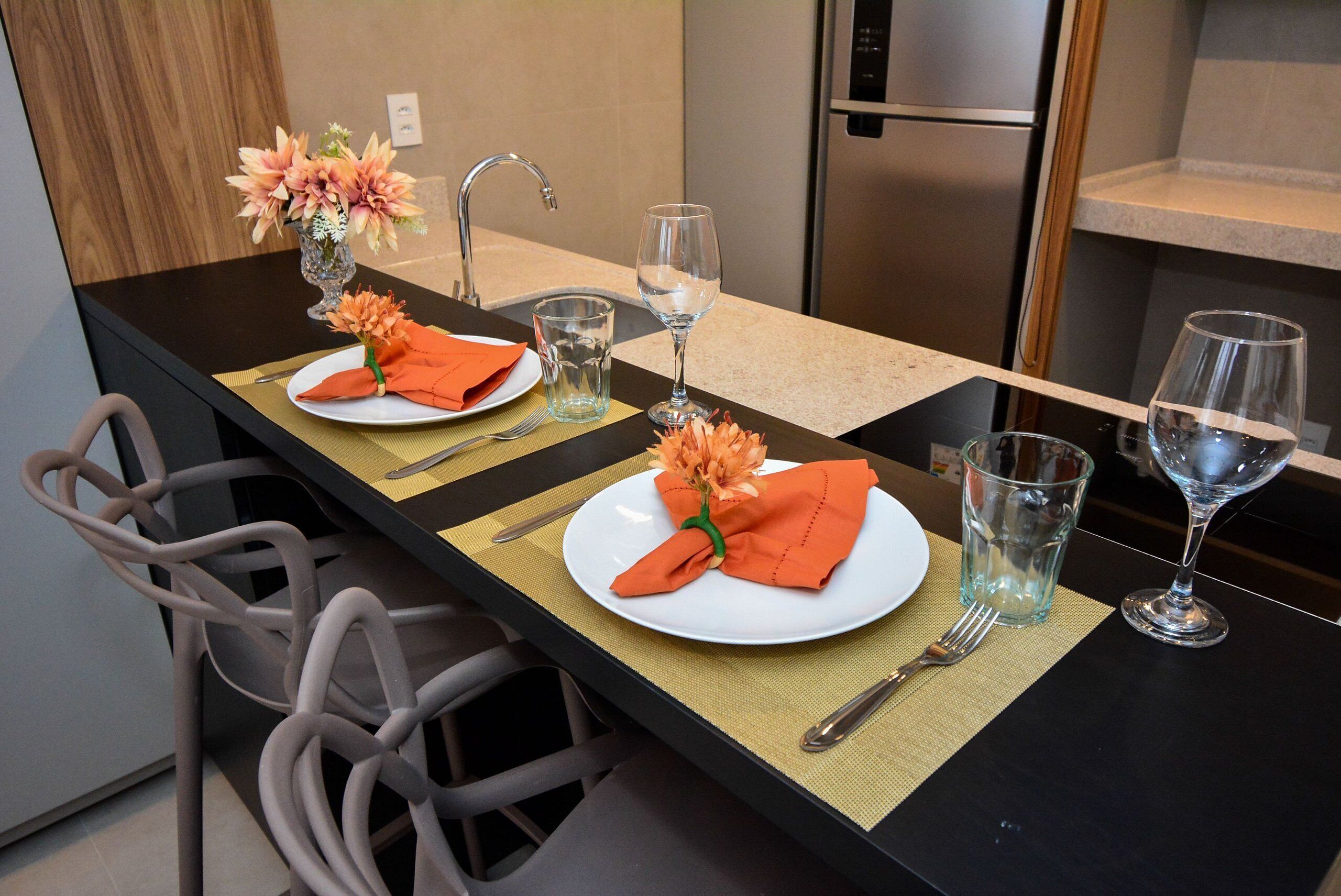 Un comptoir de cuisine aménagé en coin repas, avec deux assiettes, un vase de fleurs et deux verres à vin.