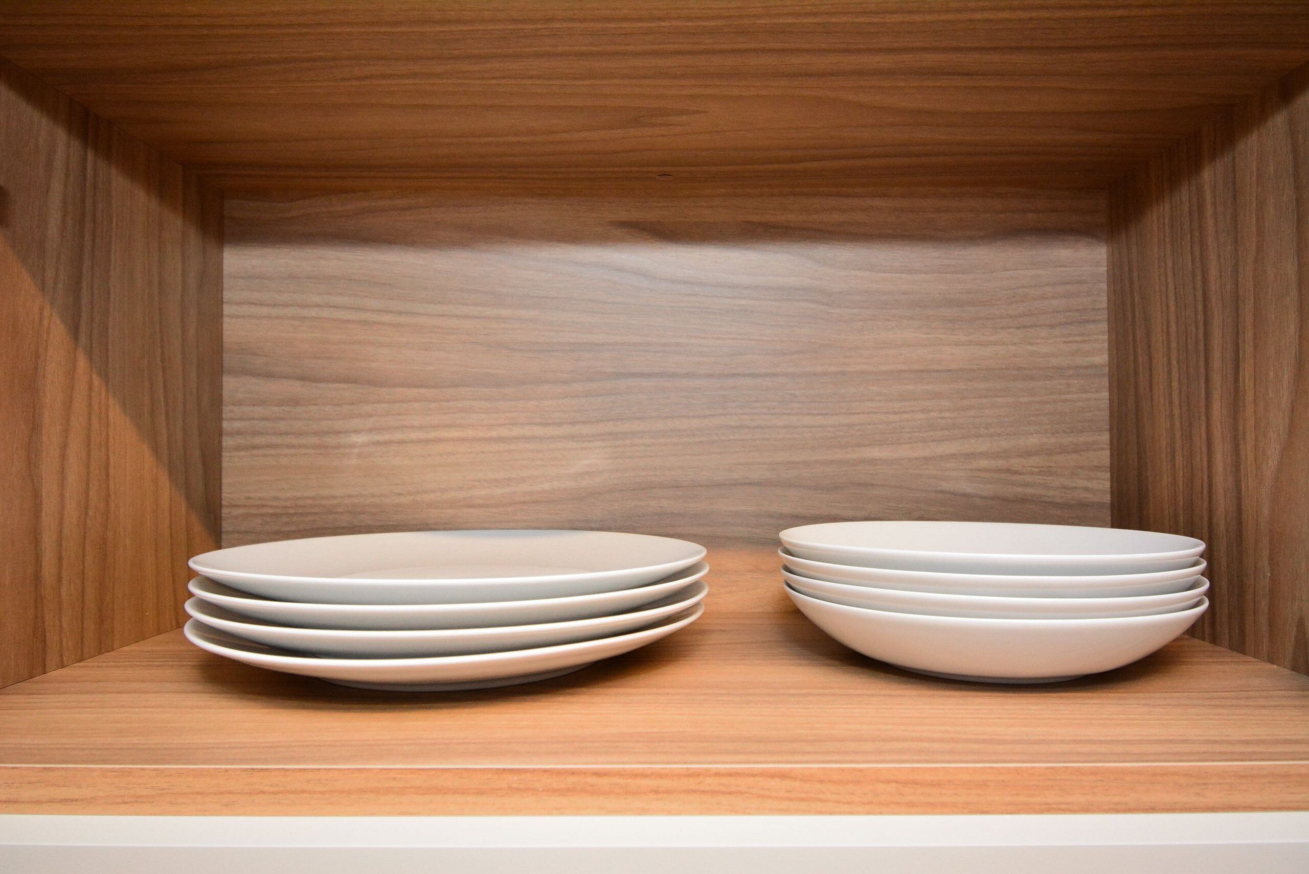 A wooden shelf with two stacks of white plates.
