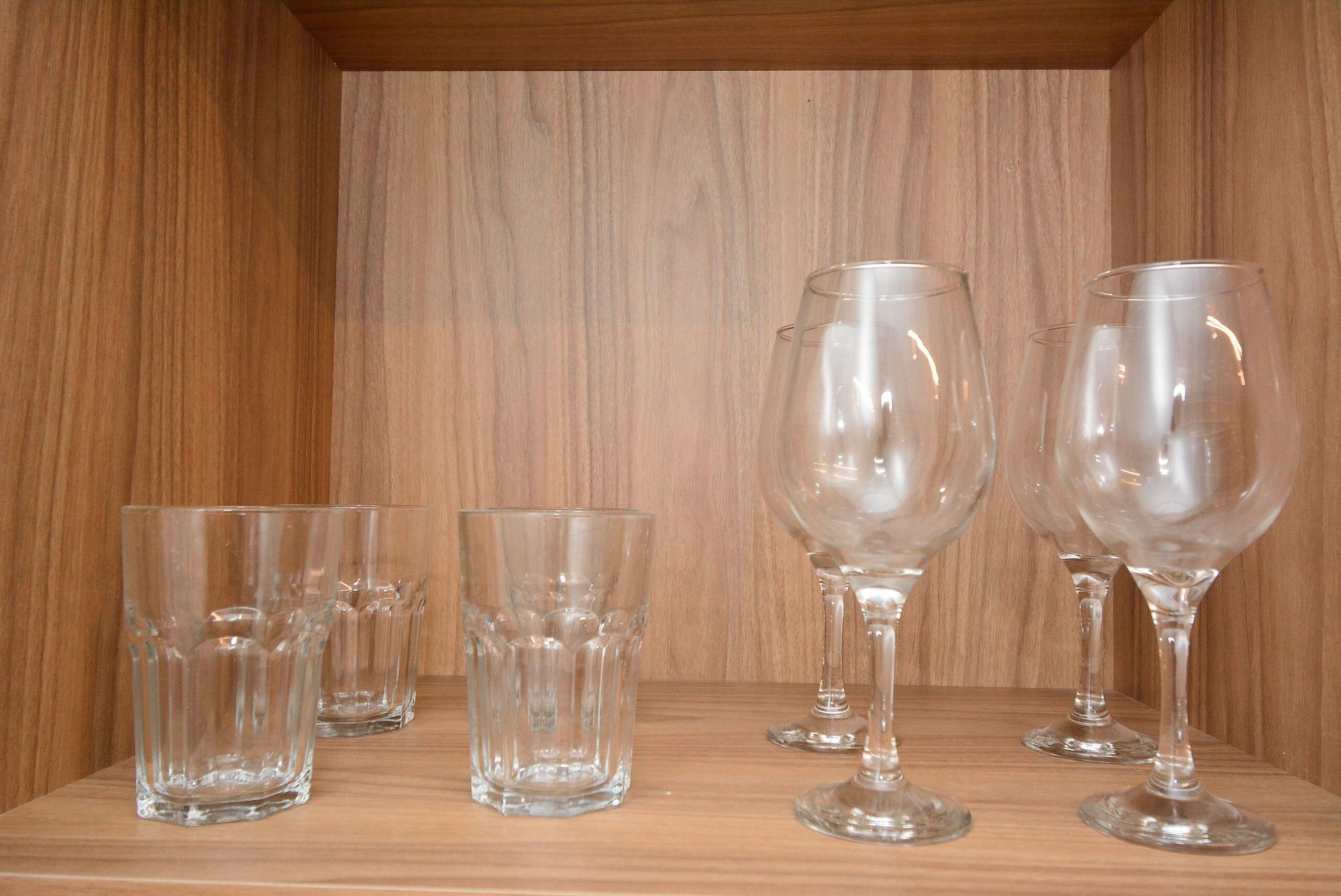 Una estantería de madera con cuatro copas de cristal para vino y dos copas de cristal para agua.