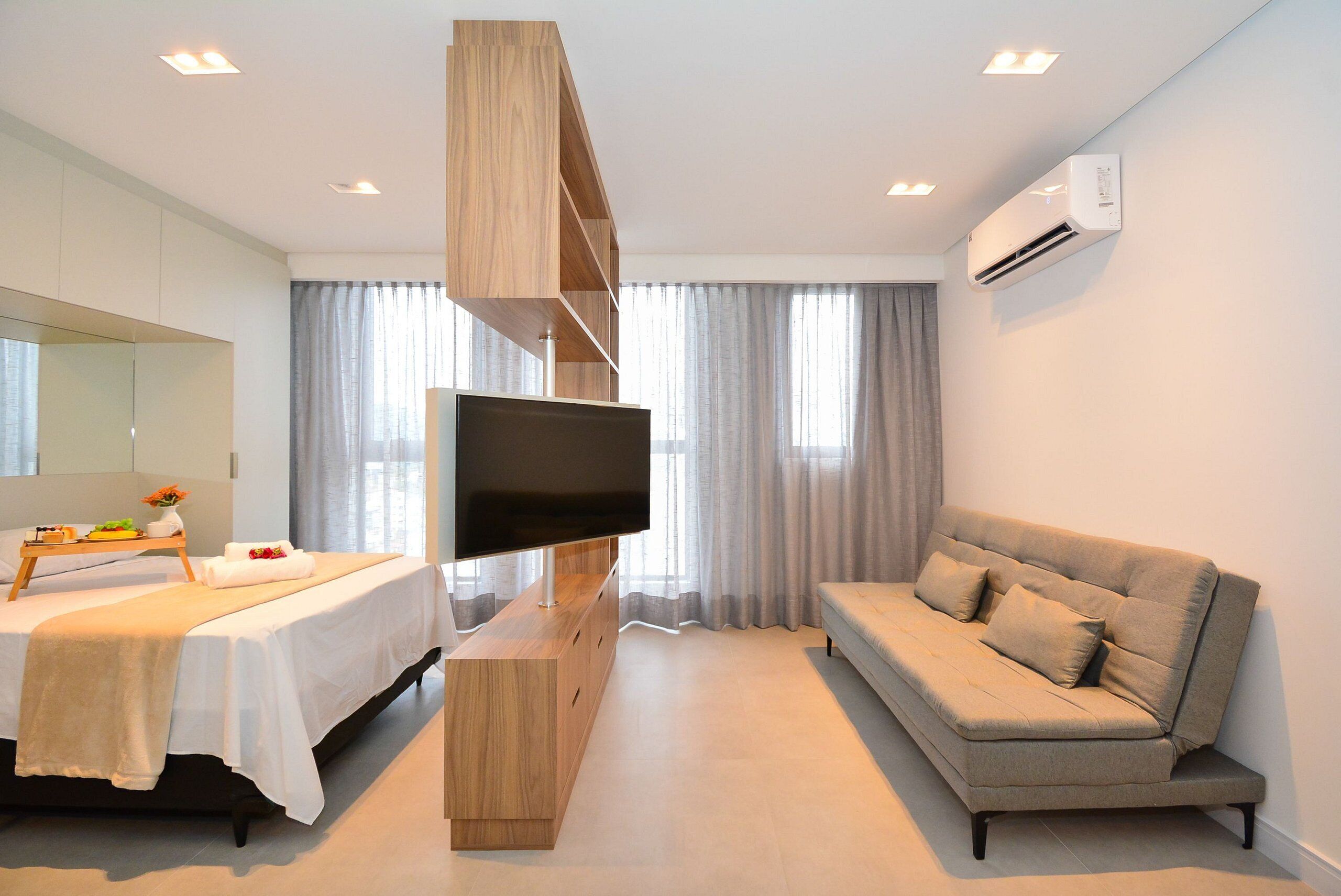 Quarto de hotel moderno com cama, sofá, televisão e aparador de madeira.