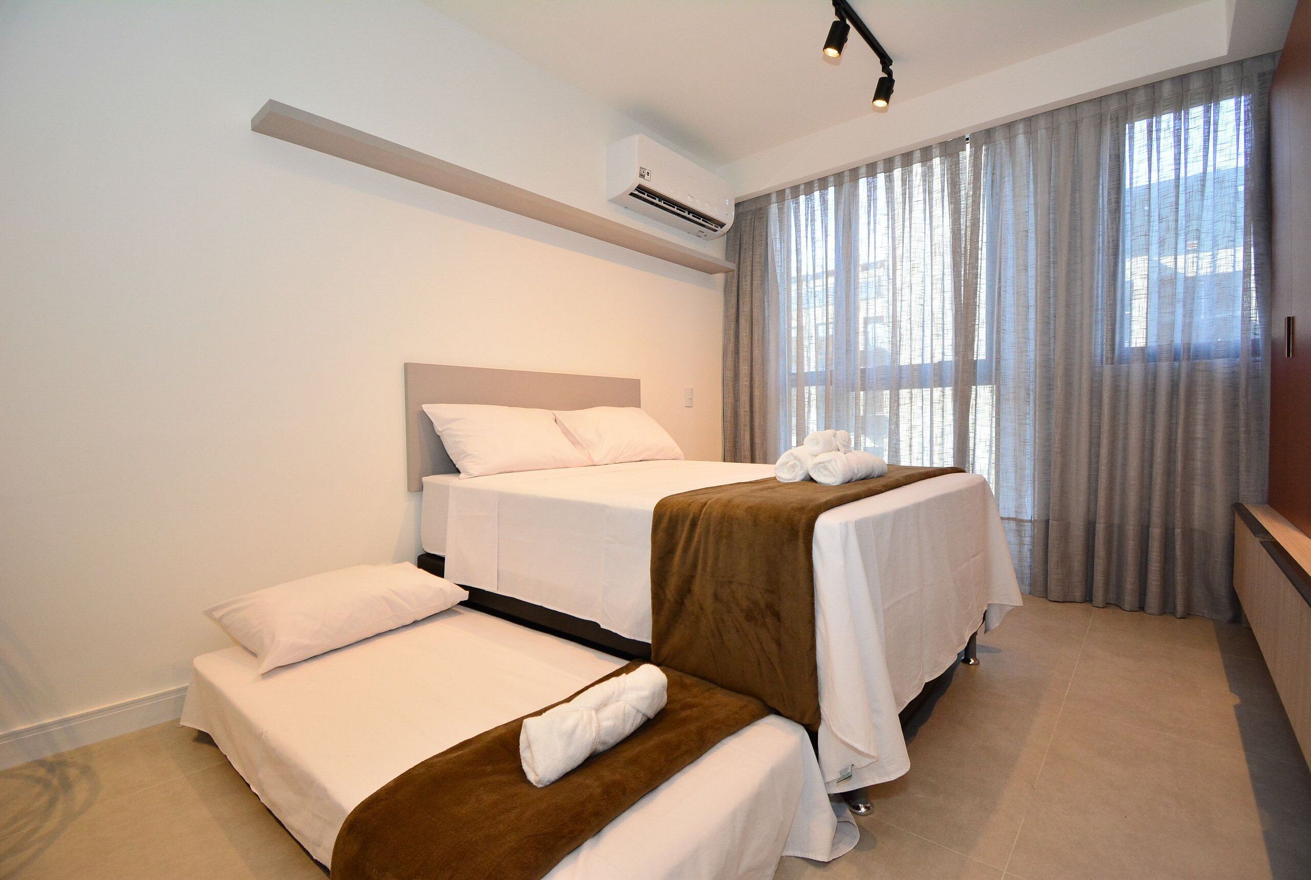 A hotel room with two beds, a ceiling fan, an air conditioning unit, and a large window with curtains.