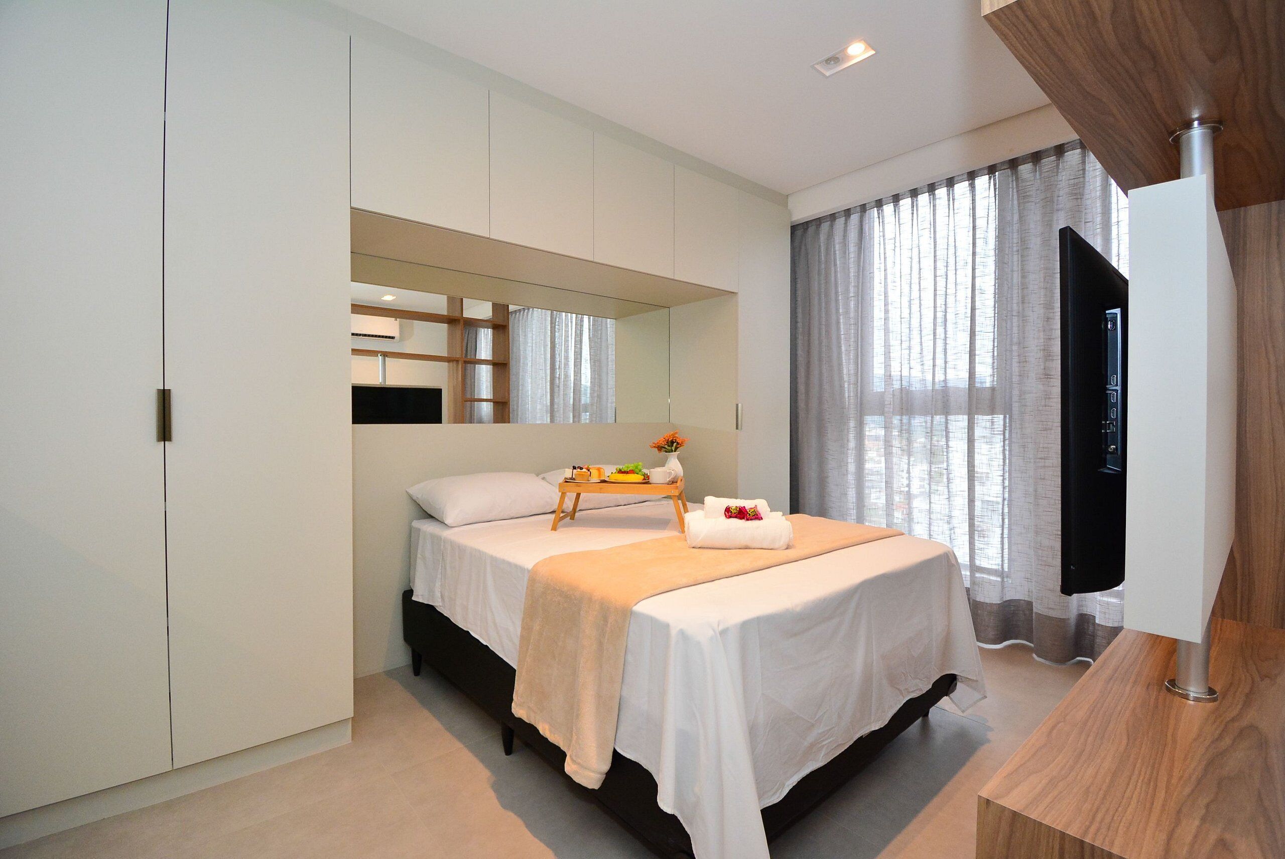 Een moderne slaapkamer met een bed, nachtkastje, spiegel en televisie.