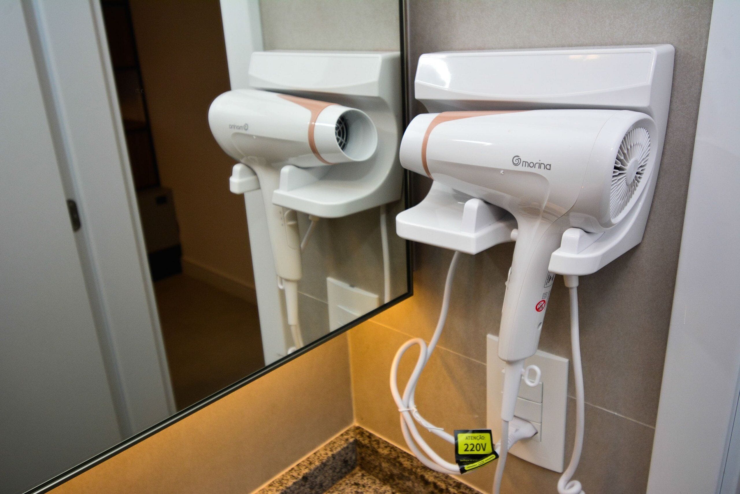 A bathroom with a mirror, two hair dryers mounted on the wall, and a 220V electrical outlet.