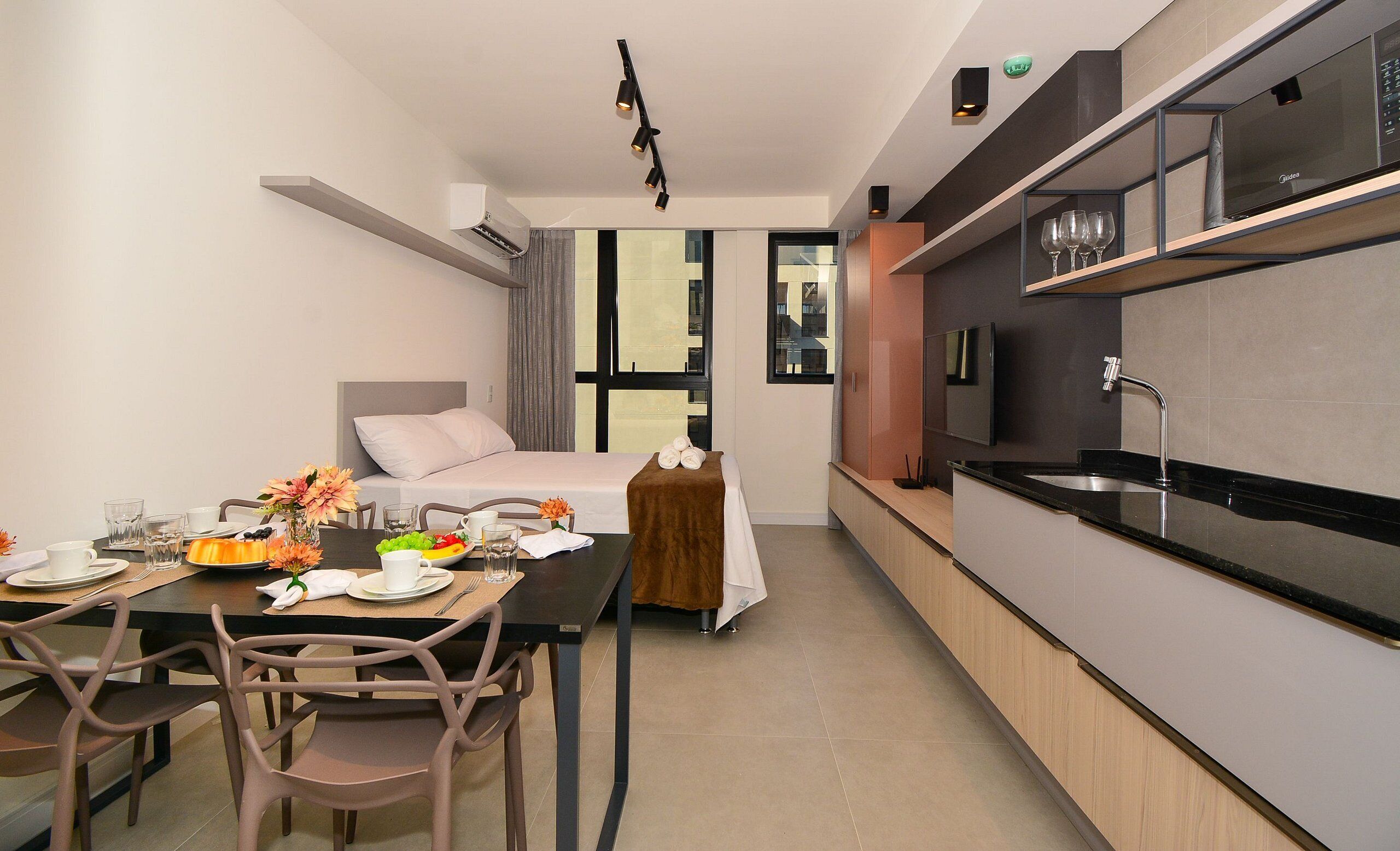 Une chambre d’hôtel moderne dotée d’un coin repas, d’une kitchenette et d’un lit avec une tête de lit.