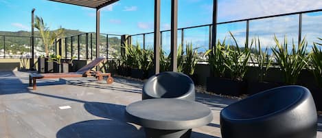 An outdoor seating area with modern chairs and a bench, surrounded by potted plants and a view of a cityscape.