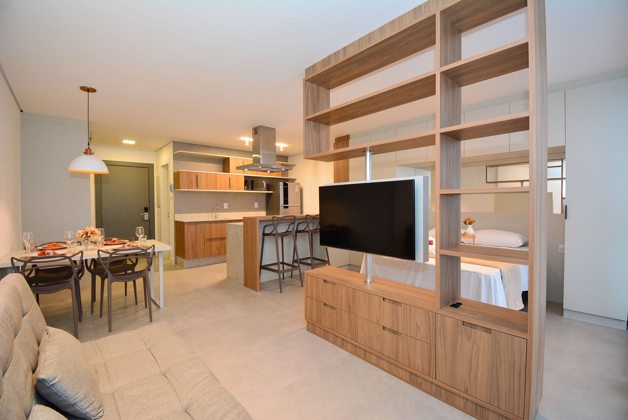 A modern living room with a TV, sofa, dining area, kitchen, and built-in shelving.