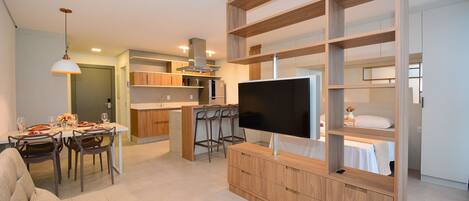 A modern living room with a TV, sofa, dining area, kitchen, and built-in shelving.