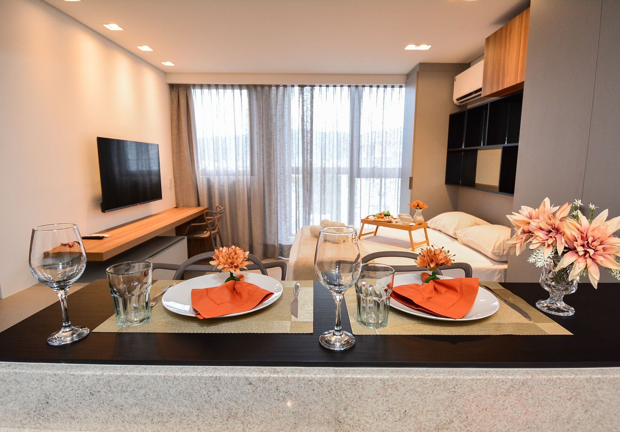Habitación de hotel con comedor, televisor de pantalla plana, sofá y ventana con cortinas.