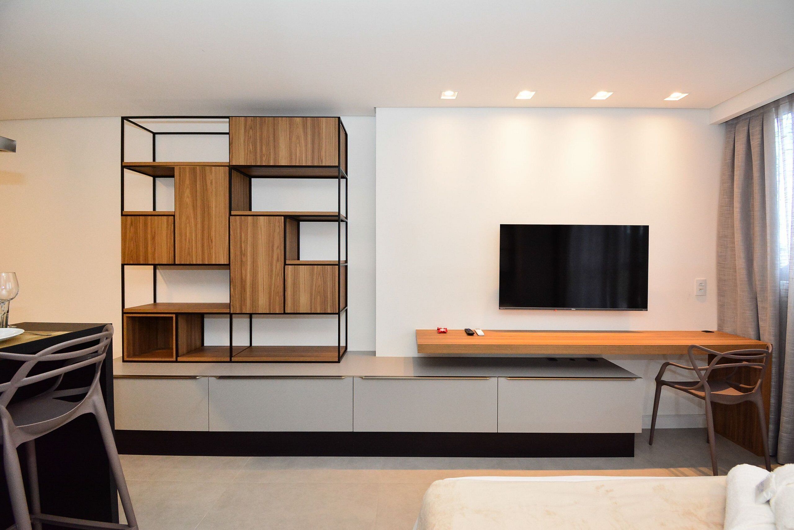 Une chambre d’hôtel moderne dotée d’un téléviseur à écran plat fixé au mur, d’une console en bois, d’un bureau intégré et d’un lit avec une tête de lit blanche.