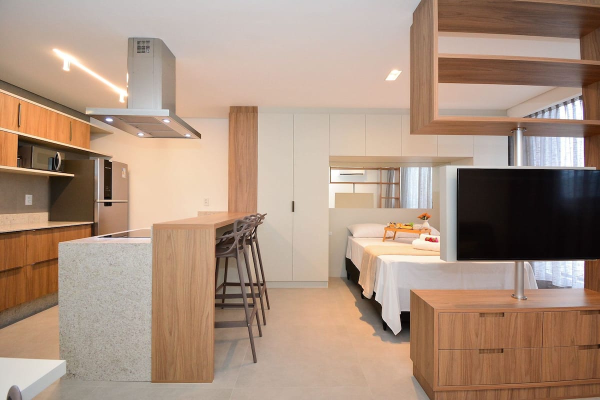 Una cocina moderna con una isla central, taburetes de bar, televisor integrado y un comedor con mesa y sillas blancas.